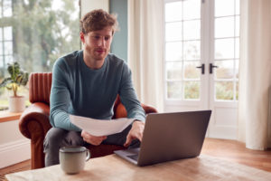 Man Sitting On Armchair At Home With Laptop Paying Bill Online - High Advice  | Assessoria Contábil em São Paulo